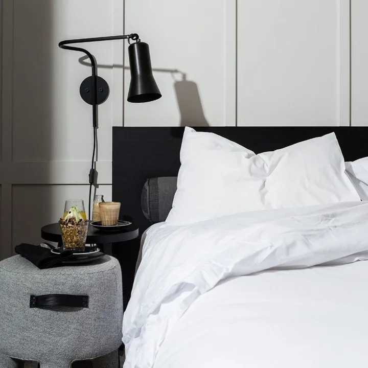 Crisp white bed linen beside a black wall lamp and a morning tray